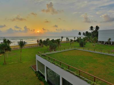 Atardecer sobre un hotel de playa con césped verde y palmeras junto al mar.