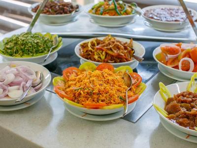 Una variedad de guarniciones coloridas en cuencos blancos en un buffet, incluyendo arroz, ensaladas y verduras.