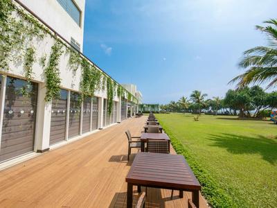 Terraza de madera con mesas y sillas junto a césped verde y edificio del hotel.