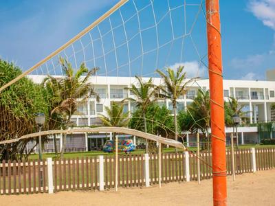 Red de voleibol de playa frente a un hotel moderno con palmeras y cielo azul.