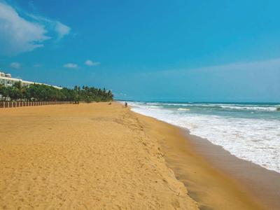 Una amplia playa de arena vacía con olas y cielo azul en un día soleado.