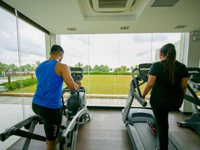 Dos personas entrenan en máquinas de cardio con vista a un área verde exterior.