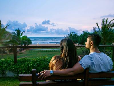 Una pareja está sentada en un banco mirando una playa tropical al atardecer.