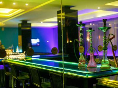 Bar moderno de hotel con mostrador iluminado con neón y varias cachimbas sobre la superficie de vidrio.