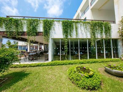 Edificio de hotel moderno con grandes ventanas de cristal y jardín cuidado bajo un cielo soleado.
