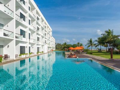 Complejo hotelero moderno con gran piscina, tumbonas y palmeras bajo un cielo azul.