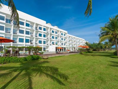 Complejo hotelero moderno con fachadas blancas, césped verde y palmeras bajo cielo despejado.
