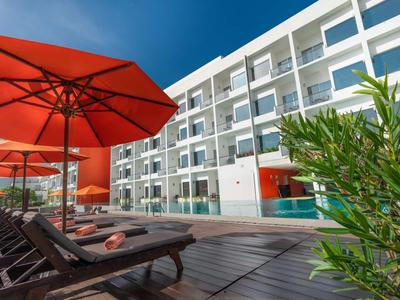 Zona de piscina moderna de hotel con tumbonas y sombrillas rojas bajo un cielo azul claro.