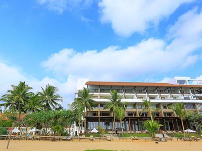 Edificio moderno di un hotel con balconi, palme e spiaggia sabbiosa sotto un cielo azzurro.