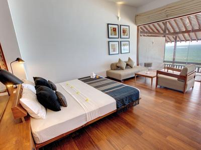 Camera d'albergo moderna con letto matrimoniale, area salotto, pavimento in legno e balcone con vista mare.