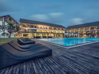Hotel met verlicht zwembad en ligstoelen op houten terras in de avond.