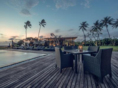 Abendliche Poolterrasse mit Stühlen und Tischen, umgeben von Palmen und ruhiger Atmosphäre.