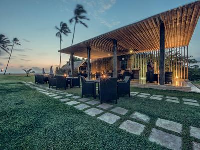Modern restaurant aan zee met zitplaatsen buiten en palmbomen bij zonsondergang.