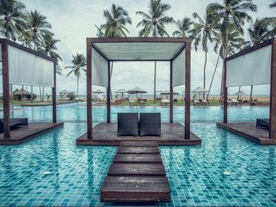 Luxuriöser Pool mit Daybeds und Palmen im Hintergrund in einem Resort.