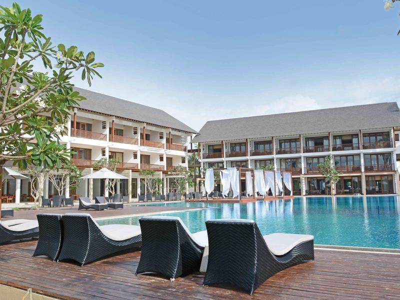 Modern hotelzwembad met ligstoelen en twee gebouwen onder een heldere lucht