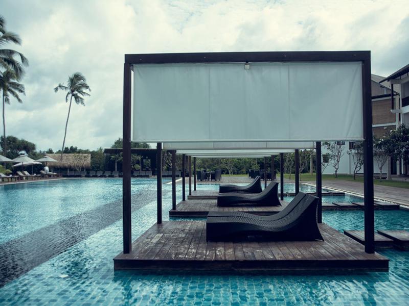 Zwembad met ligbedden onder een baldakijn en palmbomen op de achtergrond