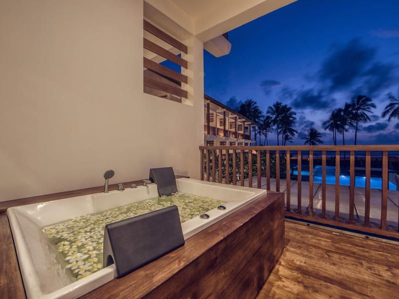 Bubbelbad op een terras met uitzicht op een zwembad en palmbomen bij schemering