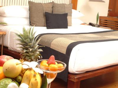 Helles Schlafzimmer mit großem Bett, weißen und grauen Kissen, Holzmöbeln und Obstschale auf Tisch.