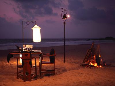 Evening beach scene with a campfire, table, and lantern in a romantic atmosphere.