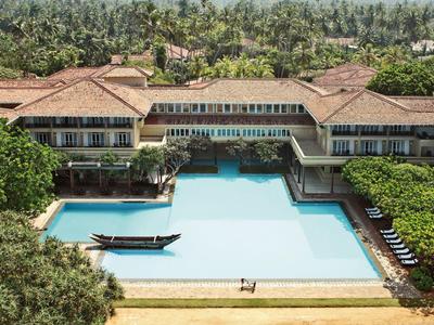 Großer rechteckiger Pool mit Steg vor Hotel mit roten Dächern, umgeben von dichtem Grün.