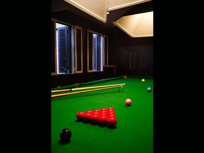 Snooker table with lined-up red balls and one white ball in a dark room with windows.