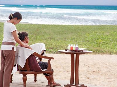 Woman receiving a massage on the beach with ocean view and drinks on a table.
