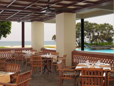 Offener Restaurantbereich mit Holztischen, Stühlen und Meerblick im Hintergrund.