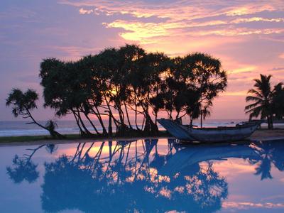 Sonnenuntergang am Meer mit Palmen und deren Spiegelung im Wasser eines Pools.