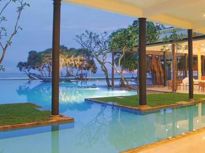 Moderner Außenpool mit überdachten Bereichen, Grünflächen und Sicht auf eine Felseninsel im Meer.