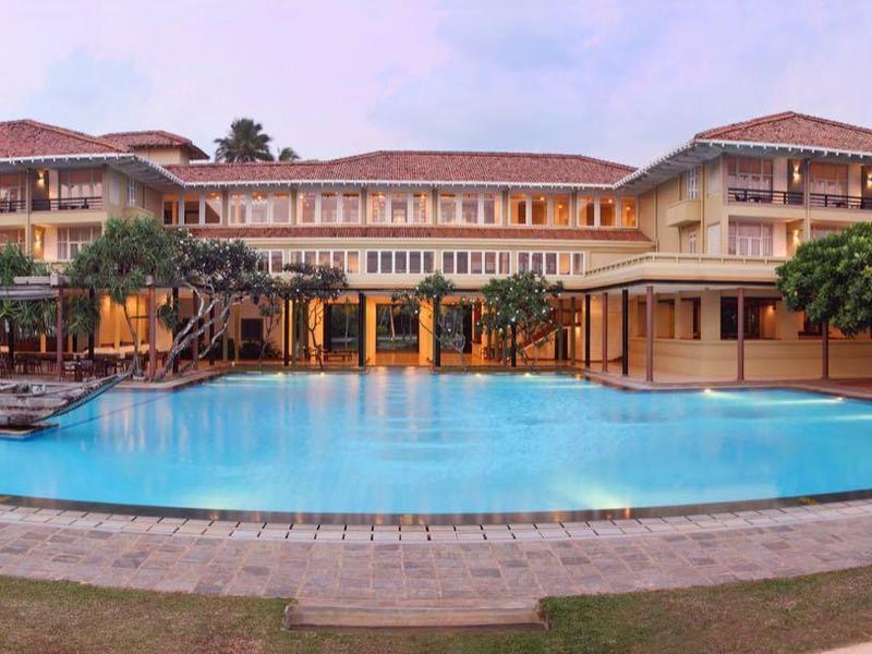 Großes Hotel mit roten Dächern, großem blauen Pool und Gartenbereich bei Dämmerung.