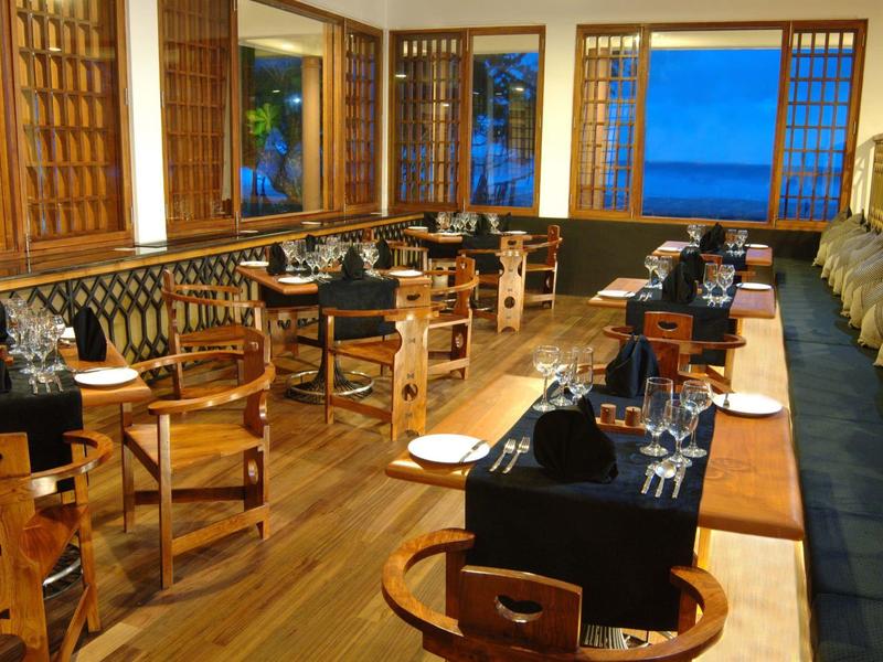 Elegantes Restaurant mit Holzboden, Holzstühlen, schwarzen Tischdecken und großem Fenster mit Meerblick.