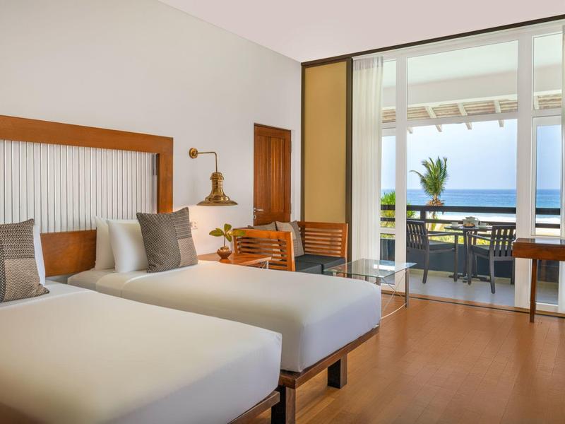 Modernes Hotelzimmer mit zwei Einzelbetten, Holzboden und Balkon mit Meerblick.