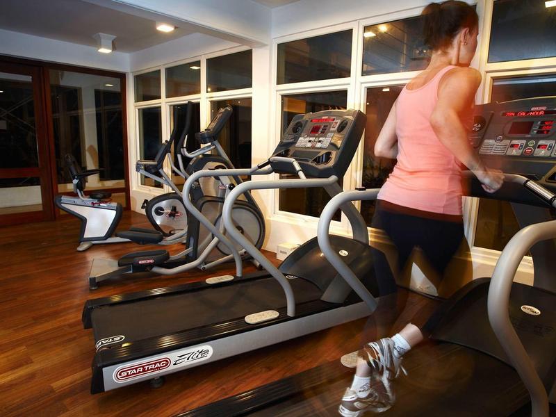 Frau läuft auf Laufband in hellem, modernem Fitnessraum mit Holzfußboden und mehreren Trainingsgeräten.