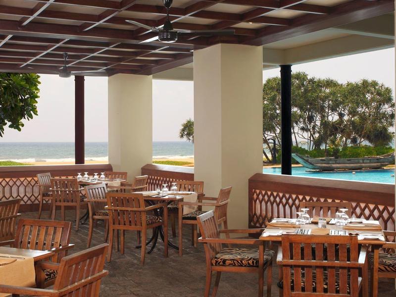 Offener Restaurantbereich mit Holztischen, Stühlen und Meerblick im Hintergrund.