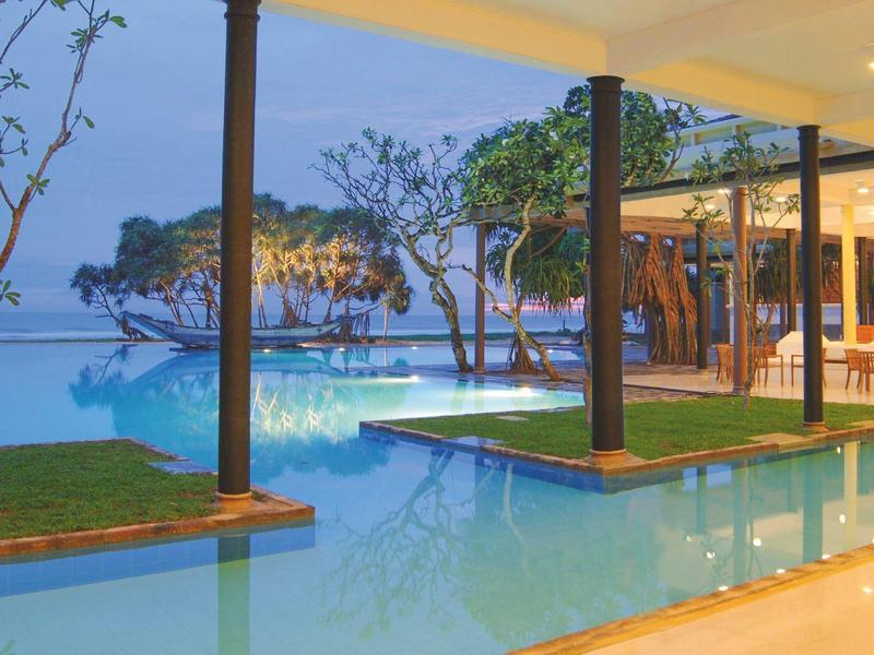 Moderner Außenpool mit überdachten Bereichen, Grünflächen und Sicht auf eine Felseninsel im Meer.