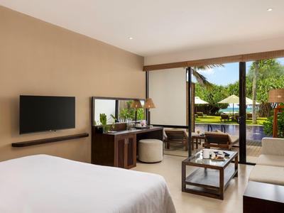 Camera d'hotel luminosa con area salotto e vista sulla piscina esterna.