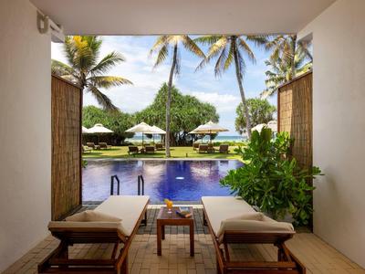 Vista da una terrazza con due lettini su una piscina e palme vicino al mare.