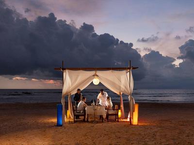 Divano romantico sulla spiaggia sotto un baldacchino al tramonto con nuvole scure.