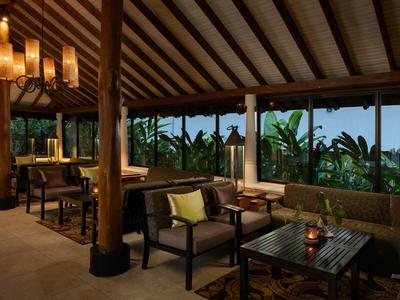 Accogliente area lounge dell'hotel con mobili in legno e grandi finestre che si affacciano su piante verdi.