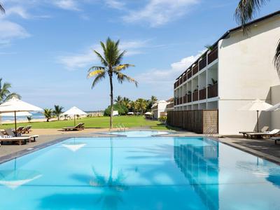 Moderner Hotelpool mit Liegestühlen und Palmen unter blauem Himmel.