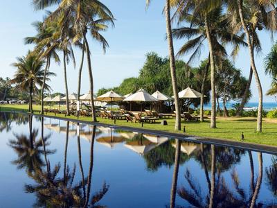Palme affiancano una piscina tranquilla con sedie a sdraio e vista sull'oceano sotto un cielo sereno.