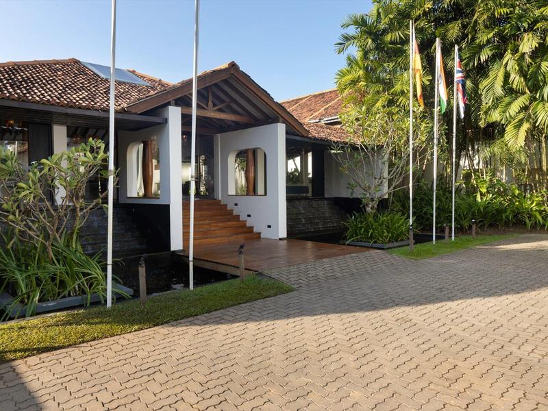 Ingresso dell'hotel con bandiere e sentiero lastricato, circondato da alberi.