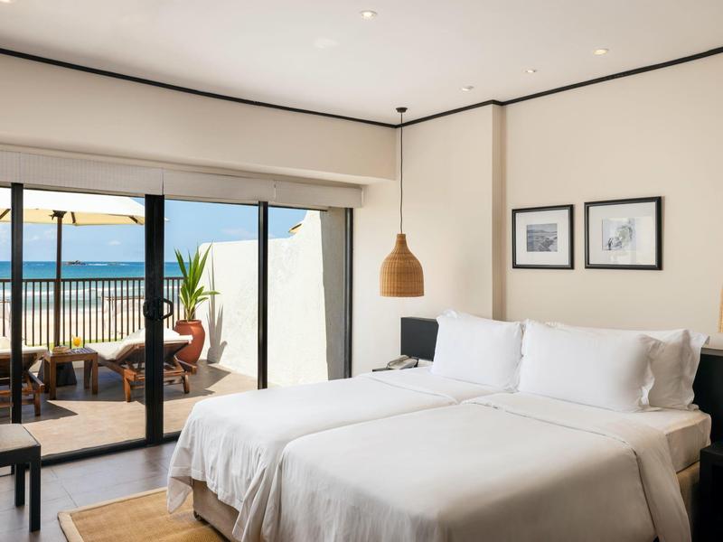 Camera d'hotel luminosa con letto matrimoniale, arredamento moderno e vista su terrazza e mare.