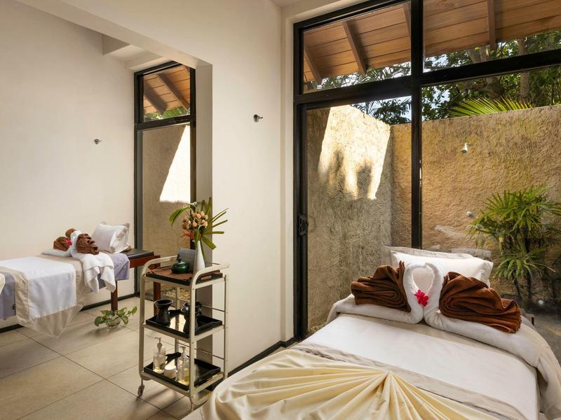 Stanza trattamento luminosa con due lettini da massaggio e grandi finestre.