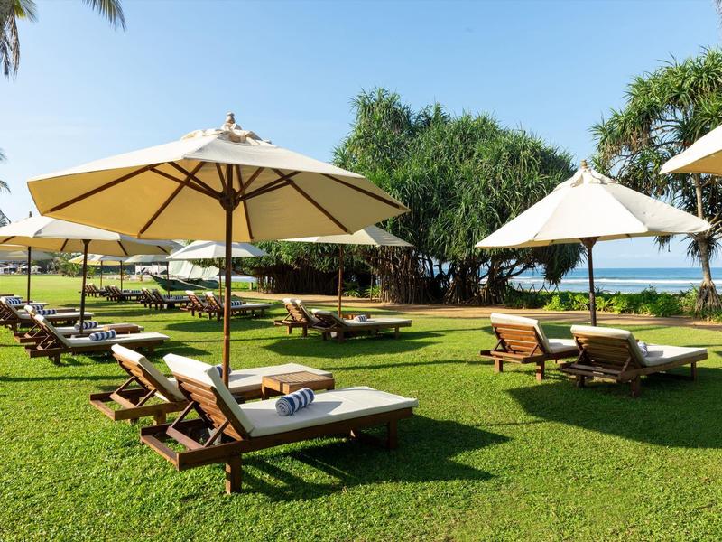 Ombrelloni e lettini su prato verde con vista oceano in una giornata di sole.