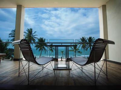 Dwa krzesła i stół na tarasie z widokiem na ocean i palmy.