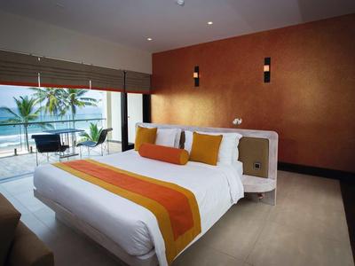 Jasny pokój hotelowy z dużym łóżkiem, pomarańczowymi akcentami i balkonem z widokiem na morze