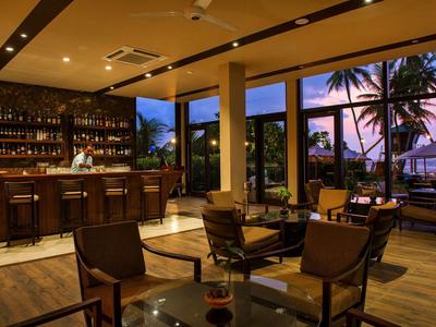 Przytulny bar hotelowy z drewnianymi meblami i widokiem na palmy o zachodzie słońca.