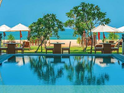 Widok na basen z leżakami i parasolami na plaży pod czystym niebem.