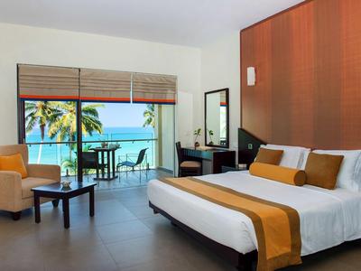 Pokój hotelowy z dużym łóżkiem i tarasem z widokiem na morze i palmy.